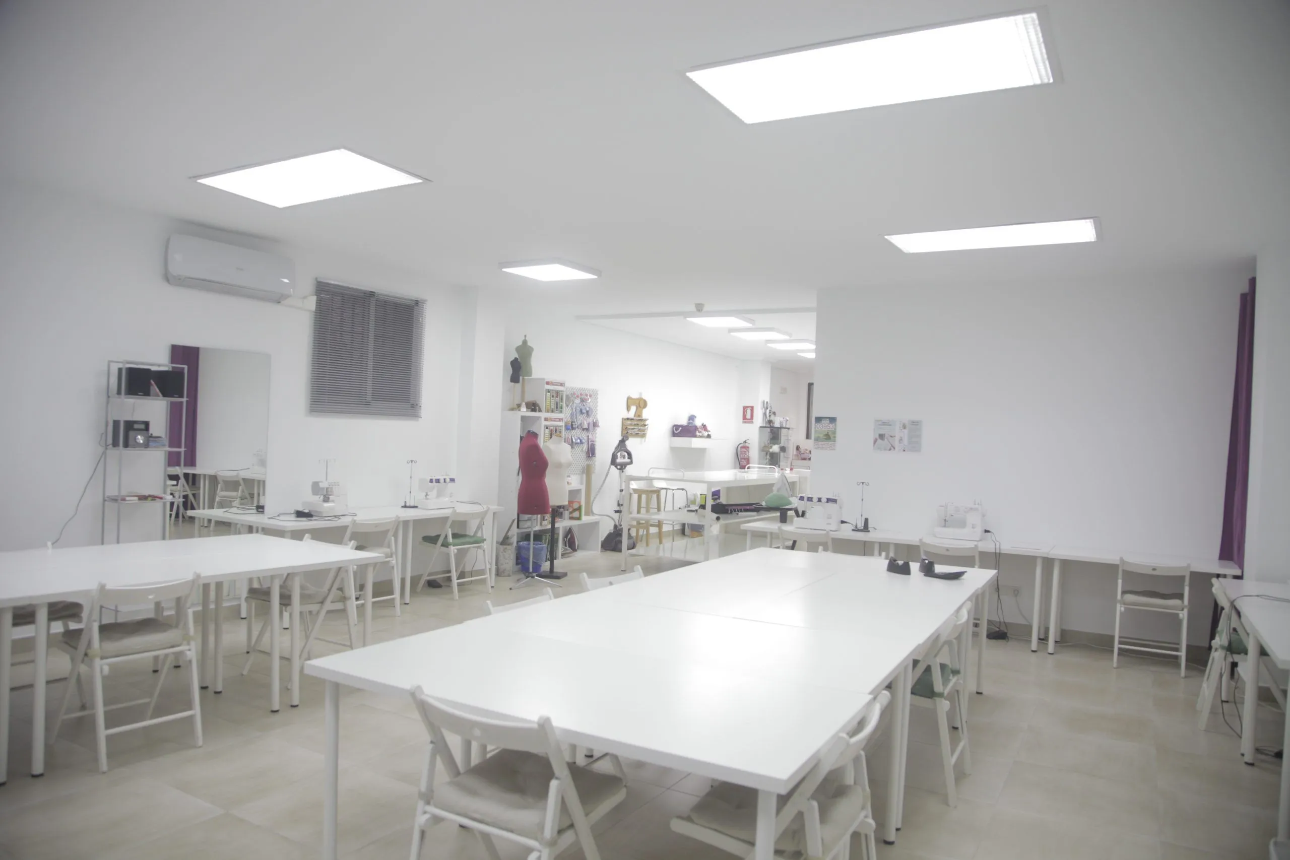 Aula de la Escuela Tresele con mesas de trabajo, máquinas de coser y maniquí