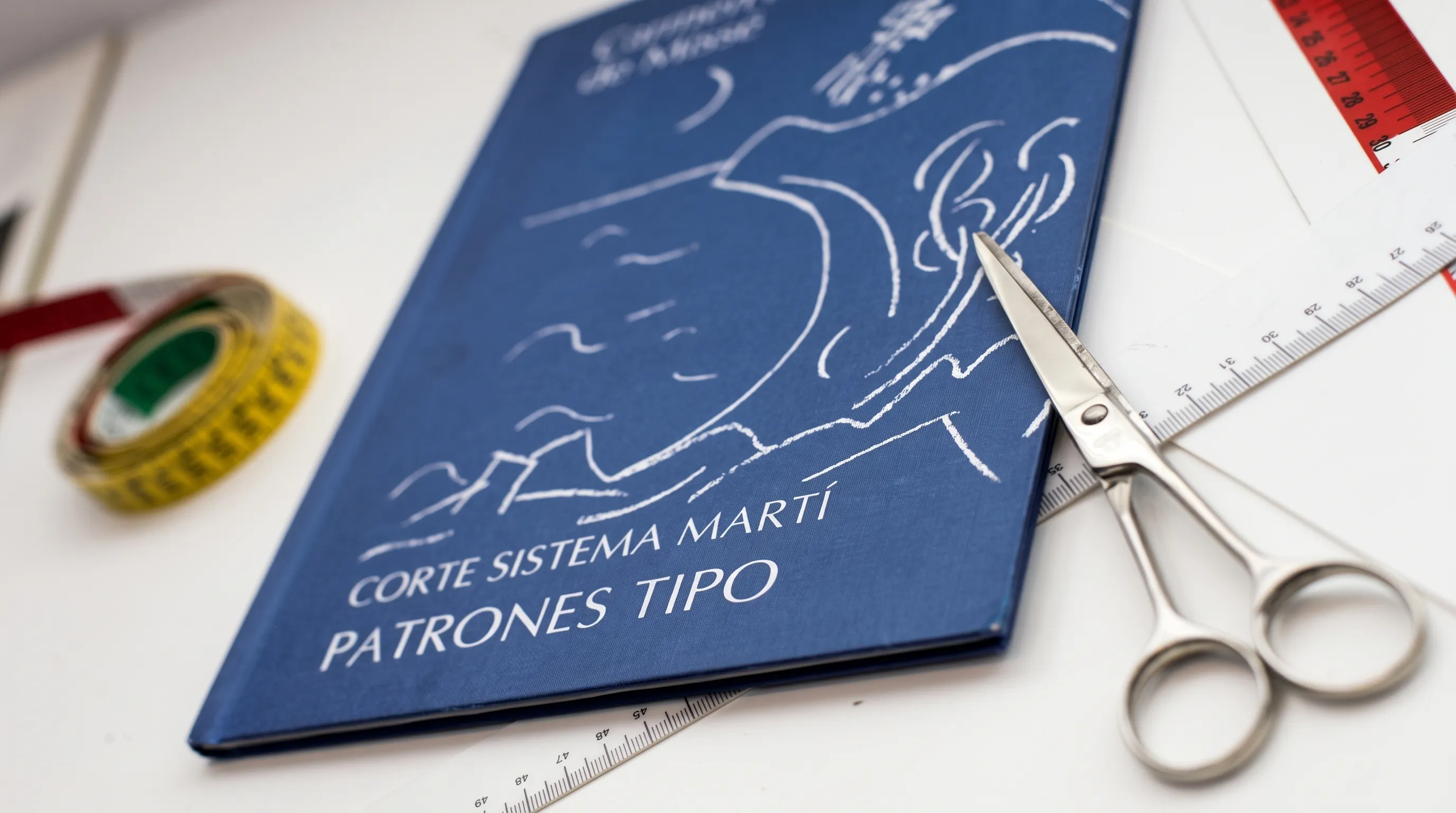 Libro de patronaje 'Corte Sistema Martí — Patrones tipo' junto a tijeras, regla y cinta métrica