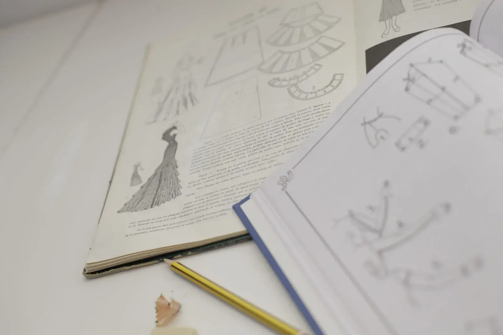 Libros de patronaje abiertos con ilustraciones de diseño de moda junto a un lápiz
