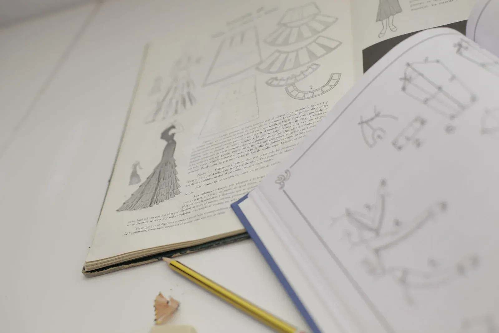 Libros de patronaje abiertos con ilustraciones de diseño de moda junto a un lápiz