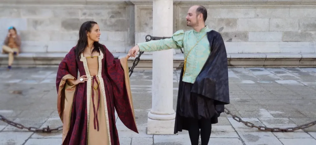 Pareja con trajes de época cervantinos confeccionados en el taller, ella con vestido burdeos y él con jubón verde y capa negra