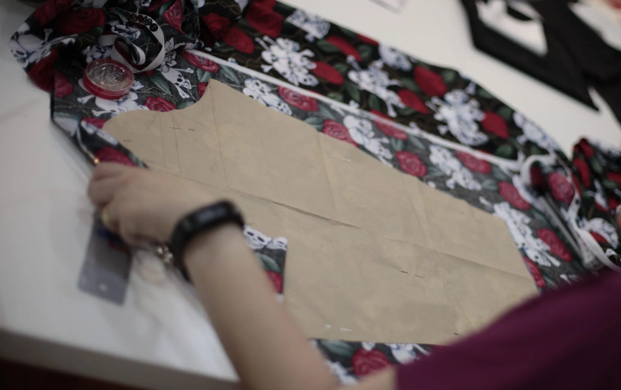 Manos prendiendo un patrón de corsé de papel kraft sobre tela estampada de rosas y calaveras