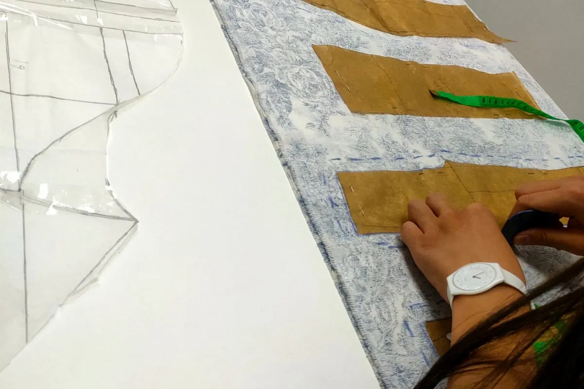 Piezas de patrón de papel sobre tela estampada azul y blanca en la mesa de trabajo del taller